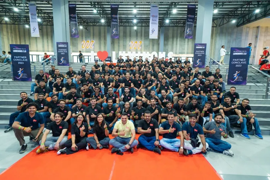Over a hundred guests in black polos seated on stadium steps at the Luminous Partner Conclave 2023