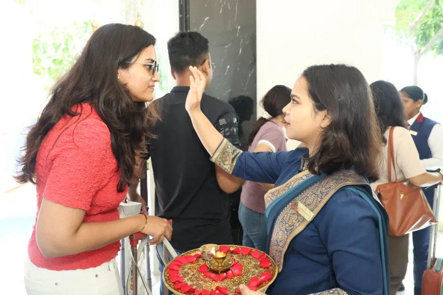 Two women welcoming a guest with a tilak and a puja thali