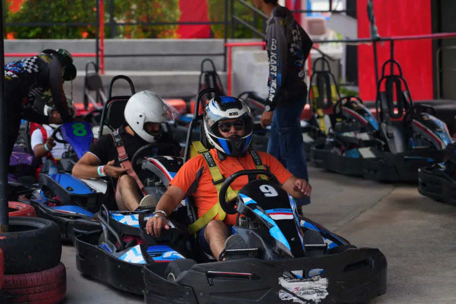 Team members in helmets strapped into go-karts at the start line