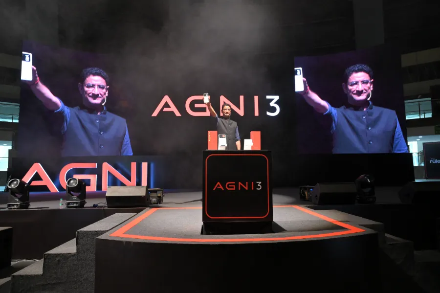 Two presenters holding up AGNI 3 phones on a dark stage