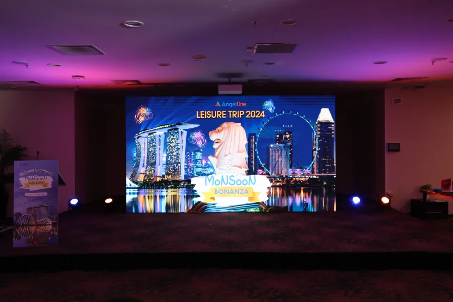 A ballroom screen reading Leisure Trip 2024 at an Angel One event