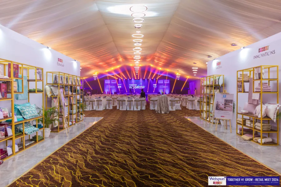A long carpeted exhibition hall lined with stalls at a Welspun event