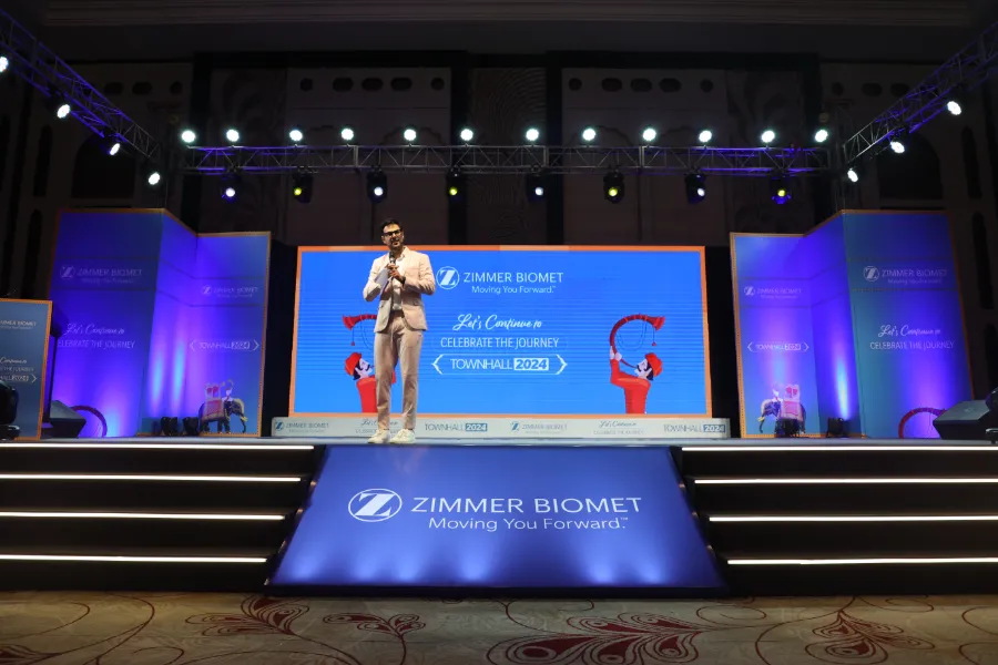 A speaker on a blue-lit stage at a Zimmer Biomet meeting